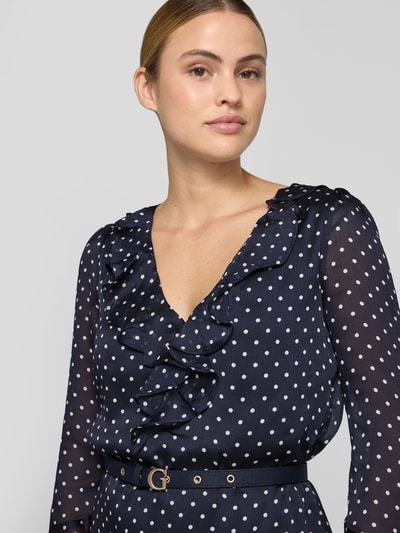 Vrouwenmodel draagt Minikleid met Rüschenbesatz van GUESS in donkerblauw met witte stippen, getailleerd, V-hals, met lange mouwen, afneembare tailleriem, context: dames mini-jurk van GUESS, met ruches, getailleerde pasvorm, afneembare tailleriem, V-hals, langärmelig design, ruglengte bij maat S: 83 cm, borstwijdte bij maat S: 42 cm, mouwlengte bij maat S: 62 cm. Nahaufnahme bovenlichaam.
