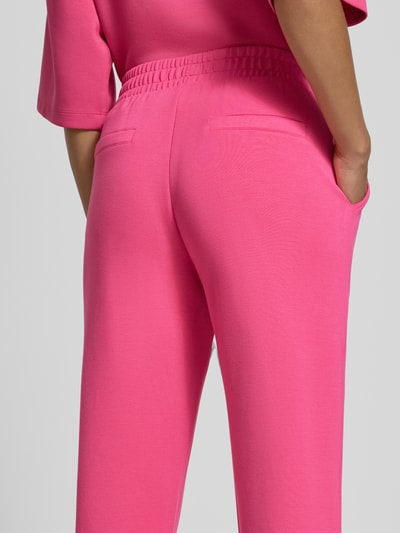 Frauenmodel trägt Sweatpants mit seitlichen Eingrifftaschen von Christian Berg Woman in kräftigem Pink, elastischer Bund, lockere Passform, angedeutete Gesäßtaschen, Nahaufnahme Rückansicht.