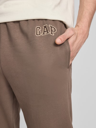 Mężczyznamodel nosi Sweatpants mit Eingrifftaschen od GAP, mieszanka bawełny, krój regular fit, wpuszczane kieszenie, logo, długość wewnętrzna nogawki w rozmiarze M 72 cm, zbliżenie na górną część nogawki.