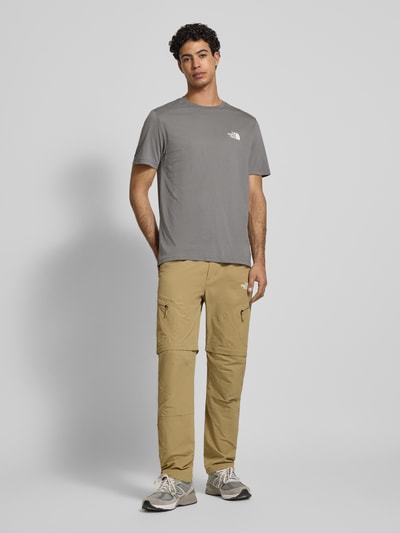 Männermodel trägt T-Shirt mit Label-Print von The North Face aus Baumwoll-Mix, Regular-Fit, grauer Farbton, Ganzkörperansicht von vorne.