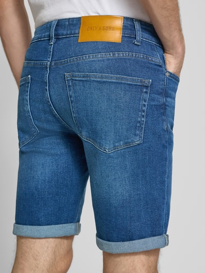 Männermodel trägt Regular Fit Jeansshorts aus Baumwoll-Mix Modell 'PLY' von Only & Sons, Denim-Optik, Label-Patch, Nieten, 5-Pocket-Design, Ganzkörperansicht Rückansicht.