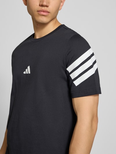 Männermodel trägt Regular Fit T-Shirt aus reiner Baumwolle von adidas Sportswear, unifarben mit Logo-Print und Kontraststreifen, Nahaufnahme Oberkörper.