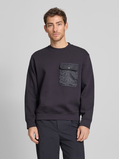 Männermodel trägt Sweatshirt mit Rundhalsausschnitt und Brusttasche von ARMANI EXCHANGE aus schwarzem Baumwoll-Mix mit Stretch-Anteil, Regular-Fit, Brusttasche vorne, Rückenlänge bei Größe M 67 cm, Ärmellänge bei Größe M 62 cm, glatte Textur, Ganzkörperansicht von vorne.