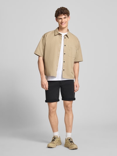 Männermodel trägt Slim Fit Jeansshorts aus Baumwoll-Mix Modell 'CK ESSENTIAL BLACK' von Calvin Klein Jeans, Denim-Optik, Label-Patch, Gürtelschlaufen, Knopf und verdeckter Reißverschluss, 5-Pocket-Design, Schwarz, Obermaterial Baumwoll-Mix, Ganzkörperansicht von vorne.