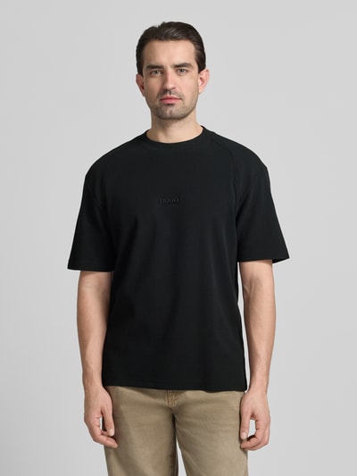 Männermodel trägt Regular Fit T-Shirt aus reiner Baumwolle Modell 'DAFFL' von HUGO, schwarz, strukturierte Jacquard-Optik, Label-Applikation, Ganzkörperansicht von vorne.
