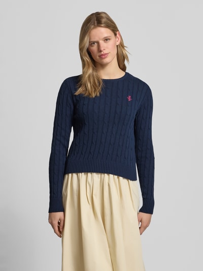 Frauenmodel trägt Strickpullover mit Zopfmuster und Label-Stitching von REVIEW in Dunkelblau, Baumwoll-Mix, Regular-Fit, Rundhalsausschnitt, Rückenlänge 52 cm, Ärmellänge 69 cm, Ganzkörperansicht von vorne.