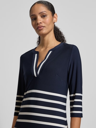 Modelka prezentuje Knielanges Kleid mit V-Ausschnitt von Christian Berg Woman Selection, mieszanka materiałów z dodatkiem streczu, krój taliowany, długość do kolan, dekolt w serek, rękaw o dł. 3/4, szerokość w rozmiarze 36: 44 cm, długość tyłu w rozmiarze 36: 92 cm, długość rękawów w rozmiarze 36: 43 cm, granatowe tło z białymi pasami, tekstura gładka, widok: zbliżenie na górną część ciała