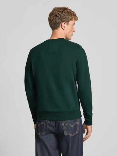 Männermodel trägt Regular Fit Sweatshirt aus Baumwoll-Mix mit Logo-Stickerei von Superdry in Dunkelgrün, Ganzkörperansicht Rückansicht.