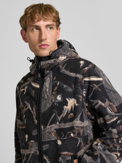 Männermodel trägt Fleecejacke mit Kapuze Modell 'Blevin' von Carhartt Work In Progress, Waldmuster, Zwei-Wege-Reißverschluss, Nahaufnahme Oberkörper.