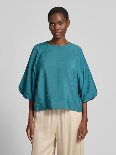 Frauenmodel trägt Regular Fit Bluse aus Viskose-Mix mit 3/4-Arm von Christian Berg Woman in Türkis mit Rundhalsausschnitt, Ganzkörperansicht von vorne. Rückenlänge bei Größe 36: 56 cm, Ärmellänge bei Größe 36: 44 cm, glatte Textur, weite Form.