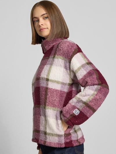 Frauenmodel trägt Regular Fit Jacke aus Teddyfell Modell 'Luca' von NOISY MAY®, kariert in Rosa, Creme und Oliv, Nahaufnahme Oberkörper. Damenjacke, Stehkragen, Reißverschluss, elastische Abschlüsse, weiche strukturierte Textur.