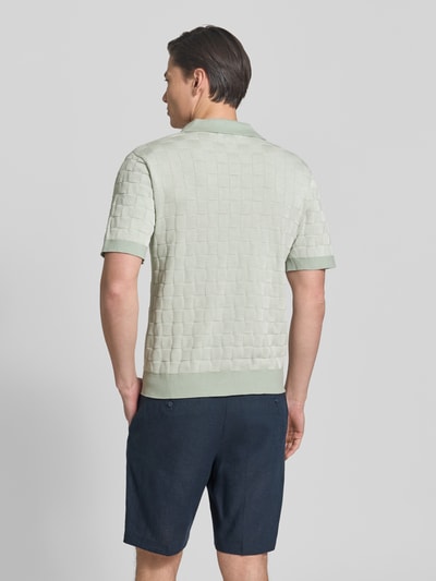 Männermodel trägt Relaxed Fit Poloshirt aus reiner Baumwolle Modell 'MILAS' von SELECTED HOMME, Gitterkaro, mehrfarbig, Strick, Ganzkörperansicht Rückansicht.