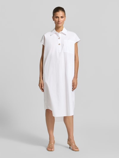 Frauenmodel trägt Knielanges Hemdblusenkleid mit kurzer Knopfleiste von Christian Berg Woman aus Reine Baumwolle, Loose-Fit, in Weiß mit Hemdblusenkragen, Brusttasche und abgerundetem Saum, Ganzkörperansicht von vorne.