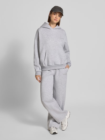 Frauenmodel trägt Sweathose in grau melange mit geradem Bein von REVIEW, Baumwoll-Mix, gerader Schnitt, elastischer Bund, Logo-Print, Ganzkörperansicht von vorne.