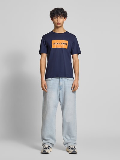 Männermodel trägt Regular Fit T-Shirt aus reiner Baumwolle Modell 'COLE' von Jack & Jones in Dunkelblau mit Label-Print, Rundhalsausschnitt, Rückenlänge bei Größe M: 70 cm, Ganzkörperansicht von vorne.