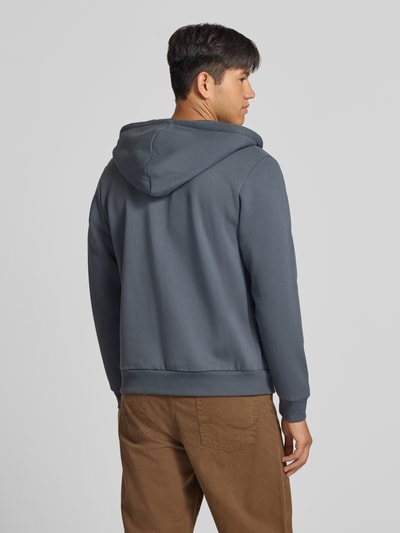 Männermodel trägt Regular Fit Sweatjacke aus Baumwoll-Mix Modell 'BRADLEY' von JACK & JONES in Grau, glatte Textur, Ganzkörperansicht Rückansicht. Sweater mit Kapuze, Tunnelzug, Kängurutasche, elastische Abschlüsse, Rückenlänge 67 cm, Ärmellänge 68 cm.