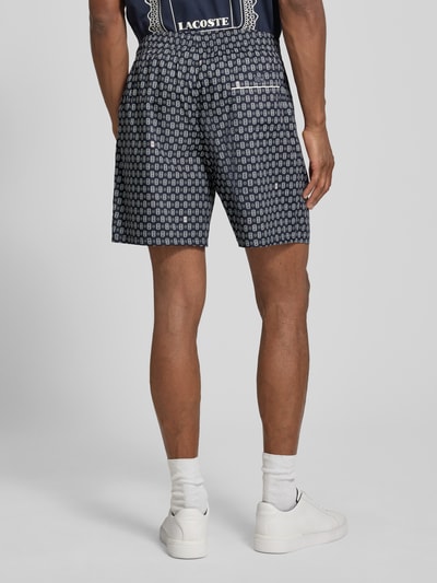 Mężczyzna nosi Regular Fit Chinoshorts aus Baumwoll-Viskose-Mix Modell 'Aop Short Tenniscourt' von Lacoste, wzór geometryczny, ciemne kolory, tekstura gładka, Herren Chinoshorts von Lacoste, Ganzkörperansicht Rückansicht.