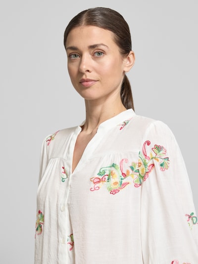 Kobieta nosi Regular Fit Bluse aus Viskose-Mix mit Stitchings od Apricot, mieszanka wiskozy, krój regular fit, hafty, dekolt w serek, długość tyłu w rozmiarze S: 57 cm, długość rękawów w rozmiarze S: 47 cm, jasne kolory, haftowane kwiatowe wzory, półzbliżenie na górną część ciała.