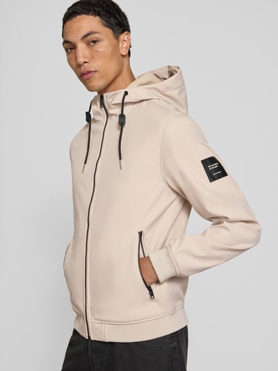 Männermodel trägt Regular Fit Jacke mit Logo-Detail von JACK & JONES in Beige, Kapuze, Reißverschlusstaschen, Softshell, Nahaufnahme Oberkörper.