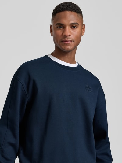 Männermodel trägt dunkelblaues Sweatshirt mit Label-Patch Modell 'Juanfrancisco' von JOOP! Collection aus Baumwoll-Mix, Nahaufnahme Oberkörper.