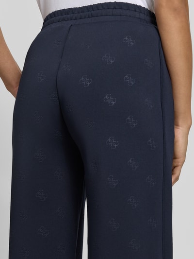 Frauenmodel trägt dunkelblaue Wide Fit Sweatpants mit Allover-Logo-Print Modell 'Calista' von Guess Activewear, Detailaufnahme Rückansicht.