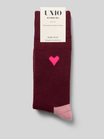 Produktfoto, Socken mit Kaschmir-Anteil und Motiv-Stitching von UNIO HAMBURG in Dunkelrot mit rosa Herz und farblich abgesetzter Spitze, Damen Socken aus Woll-Mix mit gerippten Bündchen auf hellgrauem Hintergrund.