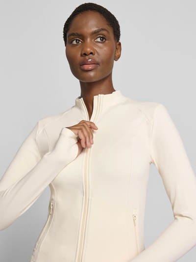 Frauenmodel trägt Jacke mit Zweiwege-Reißverschluss Modell 'Sense' von aim'n in Creme, schlanker Schnitt, glatte Oberfläche, Nahaufnahme Oberkörper. Mix mit Stretch-Anteil, Stehkragen, Reißverschlusstaschen, Kontext: Damen Jacke aim'n, Rückenlänge 52 cm, Schulterbreite 38 cm, Brustweite 42 cm, Ärmellänge 64 cm.
