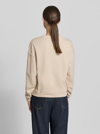 Kobiece modelka ma na sobie beżową bluzę z mieszanki bawełny MSCH Copenhagen Sweatshirt mit Label-Stitching model 'Mela Briena', luźny krój, wyhaftowane logo, okrągły dekolt, widok całej sylwetki z tyłu.