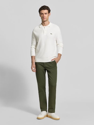 Männermodel trägt Regular Fit Poloshirt aus reiner Baumwolle von Lacoste in Weiß zu grüner Hose, Ganzkörperansicht von vorne, Herren Poloshirt von Lacoste.