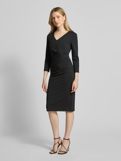 Frauenmodel trägt Knielanges Cocktailkleid mit V-Ausschnitt von Rinascimento in Schwarz, figurbetont, mit Raffungen, Material-Mix, Ganzkörperansicht von vorne.