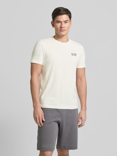 Mannenmodel draagt T-Shirt met Label-Print van EA7 Emporio Armani, wit, slim fit, katoen-elastaan, korte mouwen, voorkant, bovenlichaam close-up.
