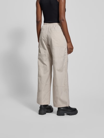 Frauenmodel trägt Stoffhose mit elastischem Bund von black palms in Beige, reine Baumwolle, lockerer Schnitt, Eingrifftaschen, Ganzkörperansicht Rückansicht.