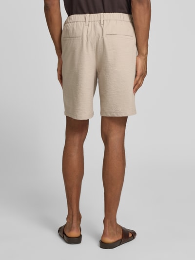 Męski model nosi Regular Fit Bermudas aus Baumwoll-Mix Modell 'KARL' od SELECTED HOMME, beżowy, seersucker, wzór w paski, tylne kieszenie, gładka tekstura. Ganzkörperansicht Rückansicht.