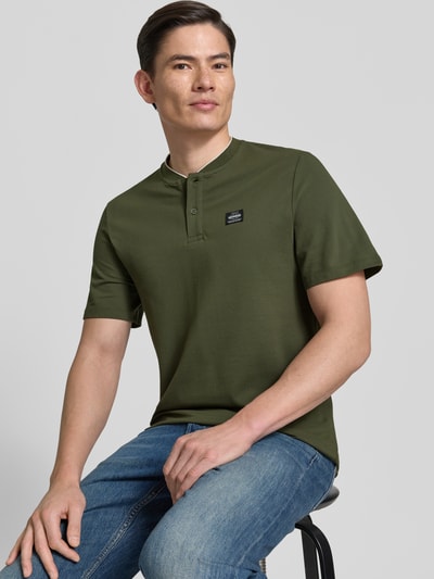 Männermodel trägt Regular Fit Poloshirt aus Baumwoll-Mix von s.Oliver RED LABEL in Olivgrün, unifarben, Piqué-Struktur, Nahaufnahme Oberkörper.