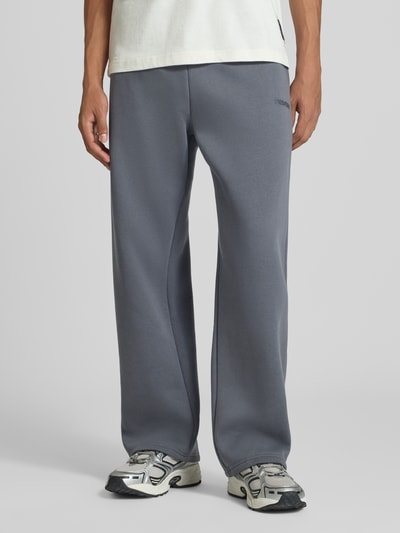 Männermodel trägt Sweatpants mit Logo-Print und Gesäßtasche von REVIEW, grauer Baumwoll-Mix, gerader Schnitt, Nahaufnahme Unterkörper.