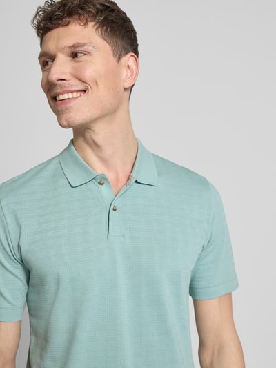 Männermodel trägt Regular Fit Poloshirt aus reiner Baumwolle von Marc O’Polo in Hellgrün mit Gitterkaro Struktur, Nahaufnahme Oberkörper.