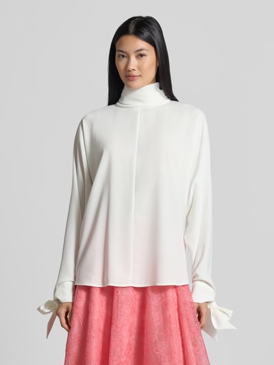 Frauenmodel trägt Relaxed Fit Langarmbluse mit Rollkragen von Emporio Armani in Weiß, leichte Stoffstruktur, Zierschleifen am Ärmel, Ganzkörperansicht von vorne.