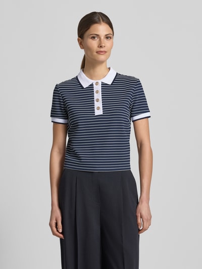 Modelka nosi koszulkę polo Cropped Poloshirt aus Viskose-Mix model 'ALPHONSINE' od Guess, mieszanka wiskozy z dodatkiem streczu, wzór w paski, listwa guzikowa, długość tyłu w rozmiarze S: 49 cm, widok całej sylwetki z przodu.