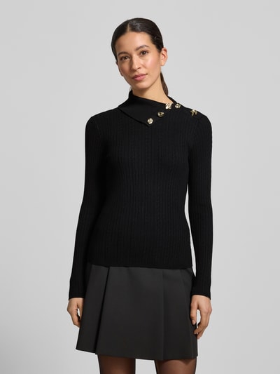 Frauenmodel trägt schwarzen Slim Fit Rollkragenpullover aus Viskose-Mix Modell 'Sicilla' von Guess mit goldfarbenem Zierbesatz, Strick-Optik, Ganzkörperansicht von vorne.