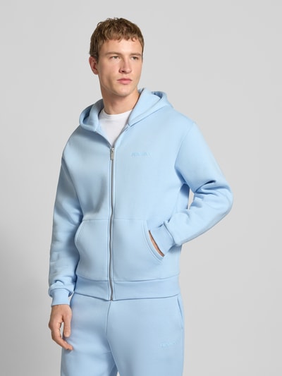 Männermodel trägt Regular Fit Sweatjacke mit Reißverschluss von Review in Hellblau, Baumwoll-Mix, Logo-Print, Kapuze, Kängurutasche, elastische Abschlüsse, Ganzkörperansicht von vorne.