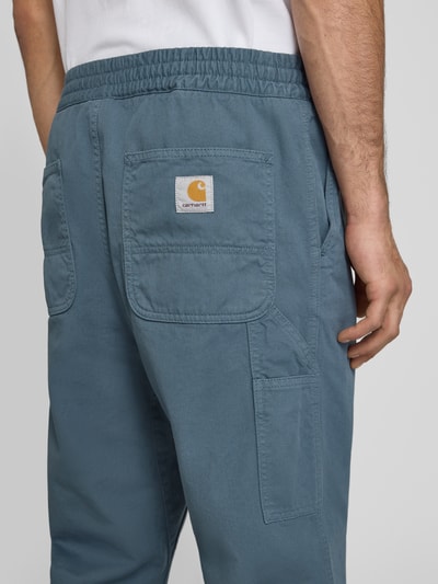 Männermodel trägt Hose mit elastischem Bund Modell 'Moraga' von Carhartt Work In Progress in Blau, Reine Baumwolle, Gesäßtaschen, Regular-Fit, Ganzkörperansicht Rückansicht.
