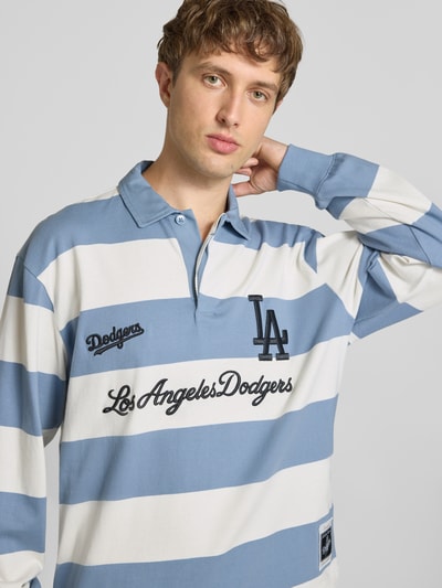 Männermodel trägt Relaxed Fit Poloshirt aus reiner Baumwolle von Champion in Blau-Weiß mit Statement-Stitching, Nahaufnahme Oberkörper. Rückenlänge bei Größe M: 71 cm, langärmeliges Design, Polokragen.