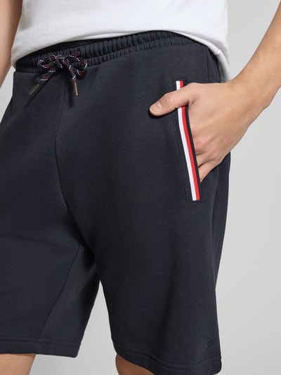 Männermodel trägt Shorts mit elastischem Bund von Christian Berg Men, dunkelblauer Baumwoll-Elasthan-Mix, Kontraststreifen, Nahaufnahme Oberschenkel.
