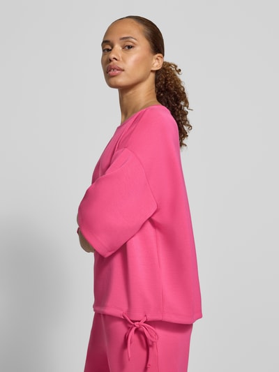 Frauenmodel trägt Oversized Fit T-Shirt aus elastischem Material-Mix von Christian Berg Woman in kräftigem Pink, Zierschleife am Saum, Halbarm, Ganzkörperansicht von vorne.