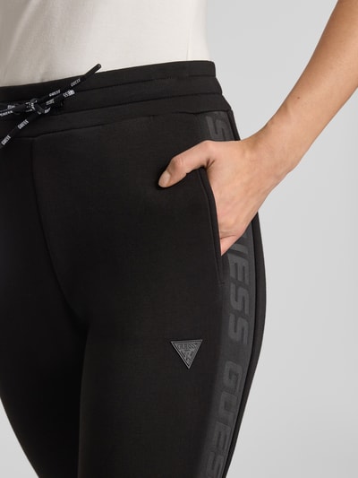 Frauenmodel trägt schwarze Sweatpants mit elastischem Bund Modell 'ALLIE' von Guess, französische Eingrifftaschen, Nahaufnahme Hüfte.