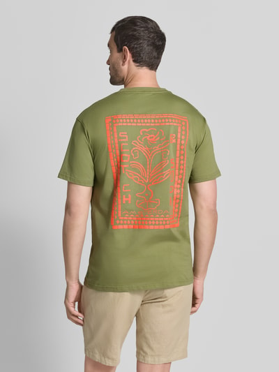 Männermodel trägt T-Shirt mit Label-Print und Rundhalsausschnitt von Scotch & Soda in olivgrün aus puur katoen, regular fit, labelprint in oranje, ruglengte maat M 72 cm, ganzkörperansicht rückansicht.