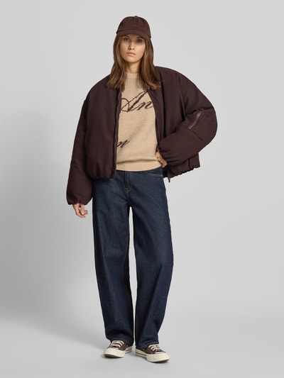 Modelka nosi bomberkę z zamkiem błyskawicznym dwustronnym od ANOTHER COTTON LAB, krój relaxed fit, stójka, wpuszczane kieszenie, kieszeń na rękawie, długość tyłu w rozmiarze S: 64 cm, szerokość ramion w rozmiarze S: 53 cm, szerokość klatki piersiowej w rozmiarze S: 60 cm, długość rękawów w rozmiarze S: 56 cm, odcień ciemnobrązowy, tekstura gładka, luźny fason, całopostaciowy widok z przodu.
