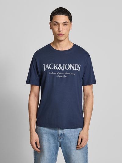 Männermodel trägt T-shirt aus katoen model 'DEVIN' van Jack & Jones in recht model met ronde hals en labelprint, heren, ruglengte bij maat M 65 cm, Ganzkörperansicht van voren.