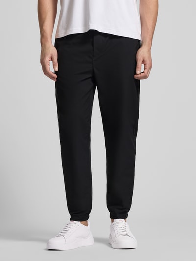 Männermodel trägt Slim Fit Schlupfhose mit Gesäßtasche von CK Calvin Klein in Schwarz, elastischer Bund, glatte Textur, Nahaufnahme Oberkörper.
