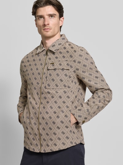 Männermodel trägt Regular Fit Jacke mit Brusttasche von Guess aus Baumwoll-Mix mit Allover-Logo-Stitching, Reißverschluss, Eingrifftaschen, Umlegekragen, Ganzkörperansicht von vorne. Rückenlänge 73 cm, Schulterbreite 45 cm, Brustweite 51 cm, Ärmellänge 65 cm bei Größe M.
